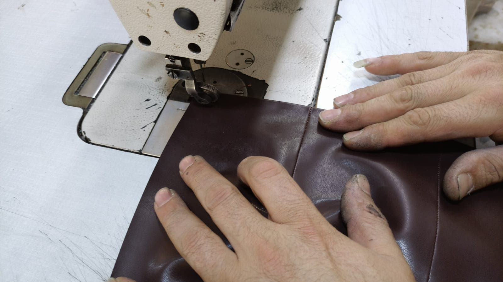 Hands guiding a burgundy leather upper through the sewing machine