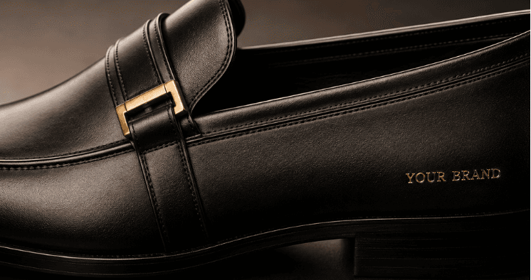 A black leather loafer with a gold brand name on the side