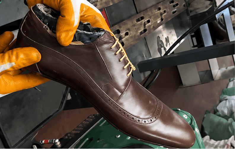A brown leather shoe held in orange inspection gloves